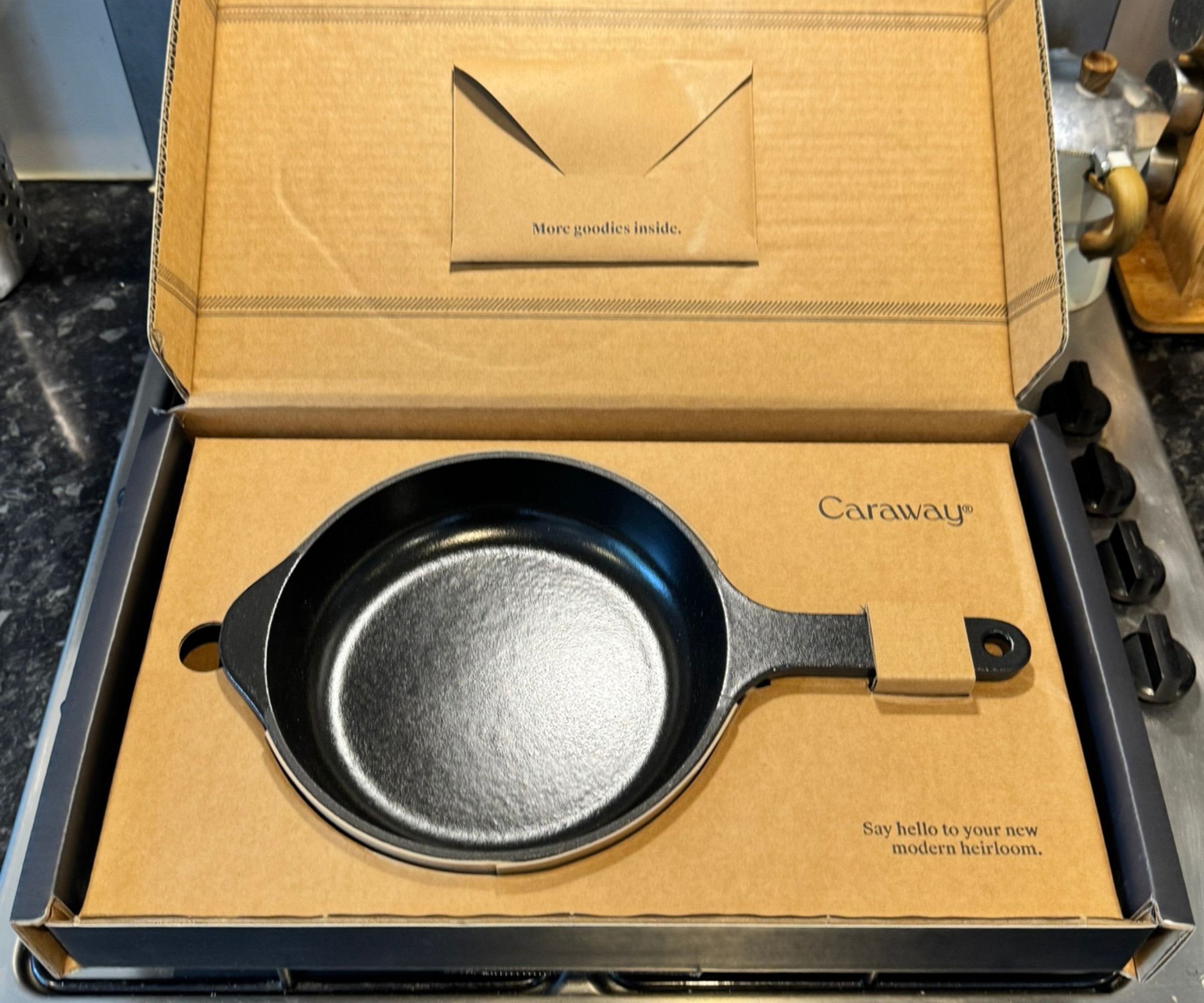 A black cast iron Caraway skillet in cardboard packaging. 