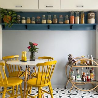 Kitchen with light blue painted walls, yellow dining table and chairs, and kitchen shelving