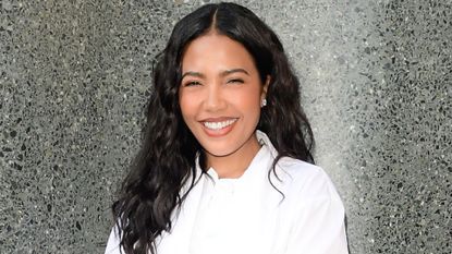 Emma Grede pictured outdoors, smiling wearing a white shirt and pearl earrings