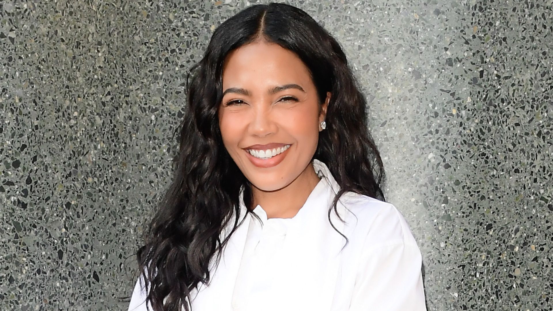 Emma Grede pictured outdoors, smiling wearing a white shirt and pearl earrings