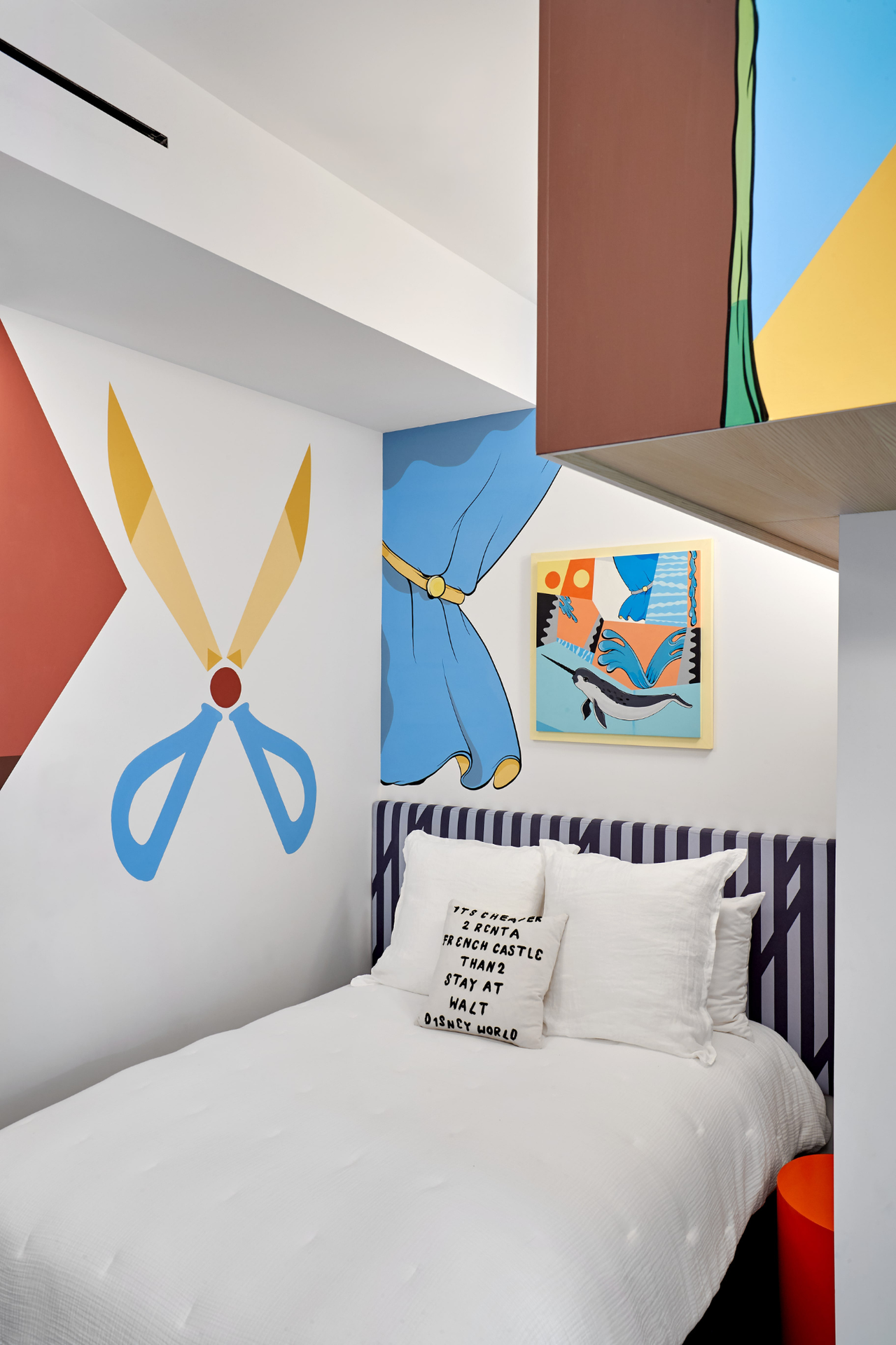 a colorful kids room in a Tribeca townhouse designed by Ghislaine Vi&ntilde;as showing the corner of the room with the bed with white bedding and white walls surrounding it covered in artwork