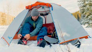 Man sitting in Eureka Mountain Pass 2 Person four-season tent pitched in snow