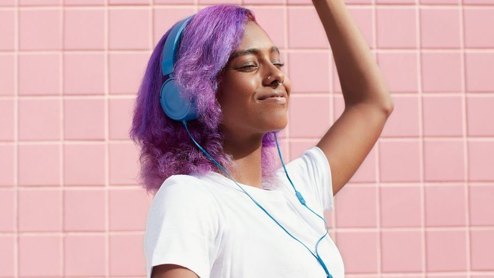 A woman with purple hair enjoying music on her blue headphones