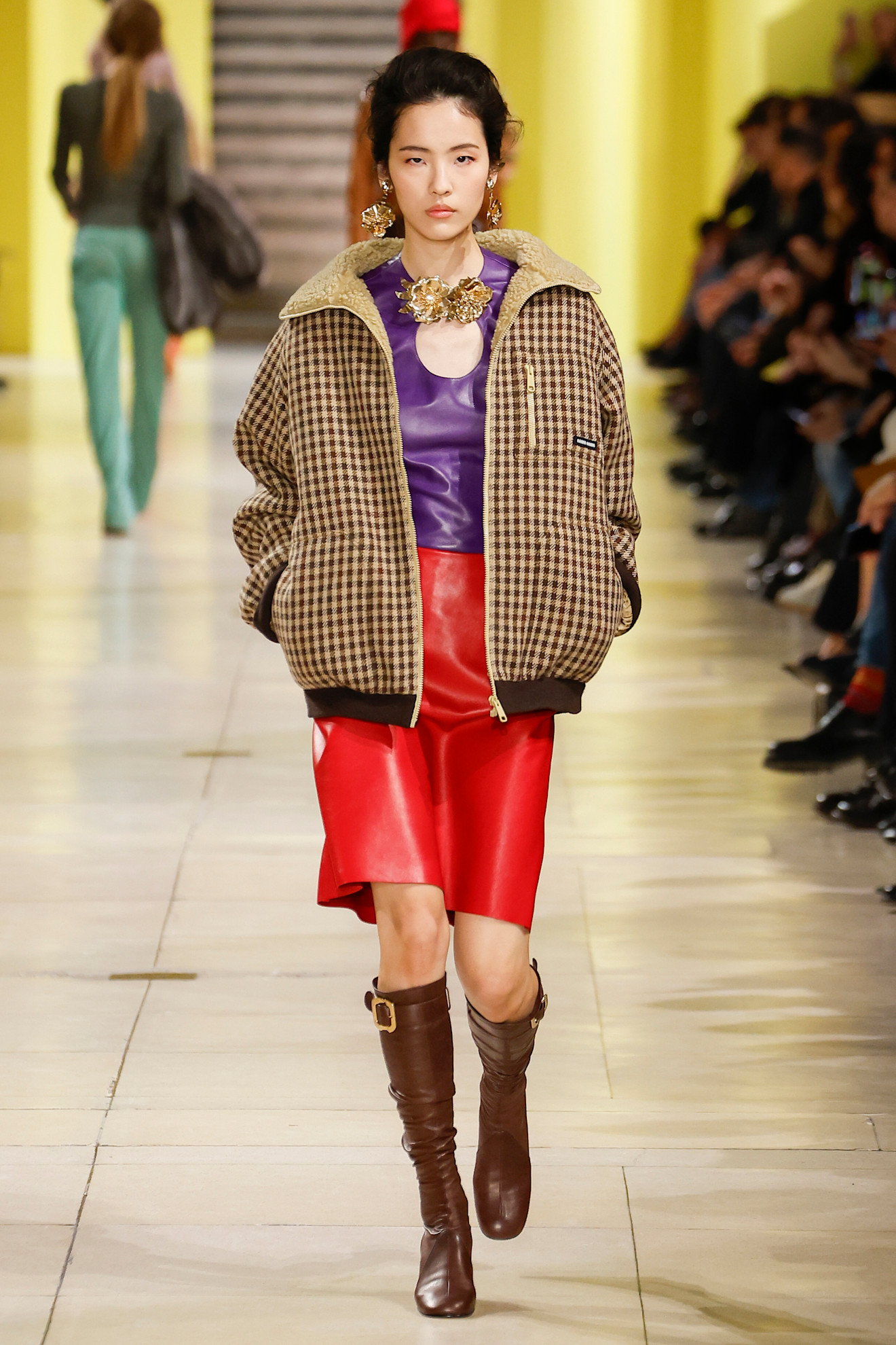 Miu Miu model walks the fall/winter 2025 runway wearing purple and red.