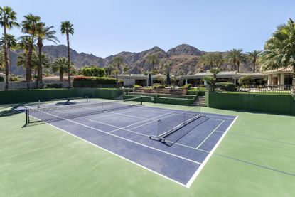 View of a full size tennis/pickleball court with mountain backdrop at a luxury, upscale estate in Indian Wells, California.