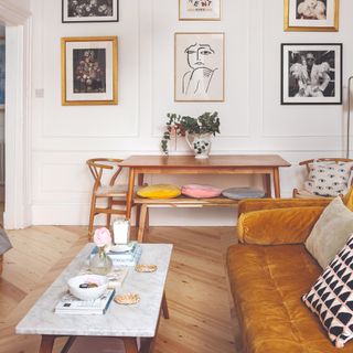 A living room with a a dining area, a gallery wall and an ochre-coloured velvet sofa