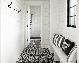 The entrance to a pool bathroom with black and white patterned tile floors and white shiplap walls