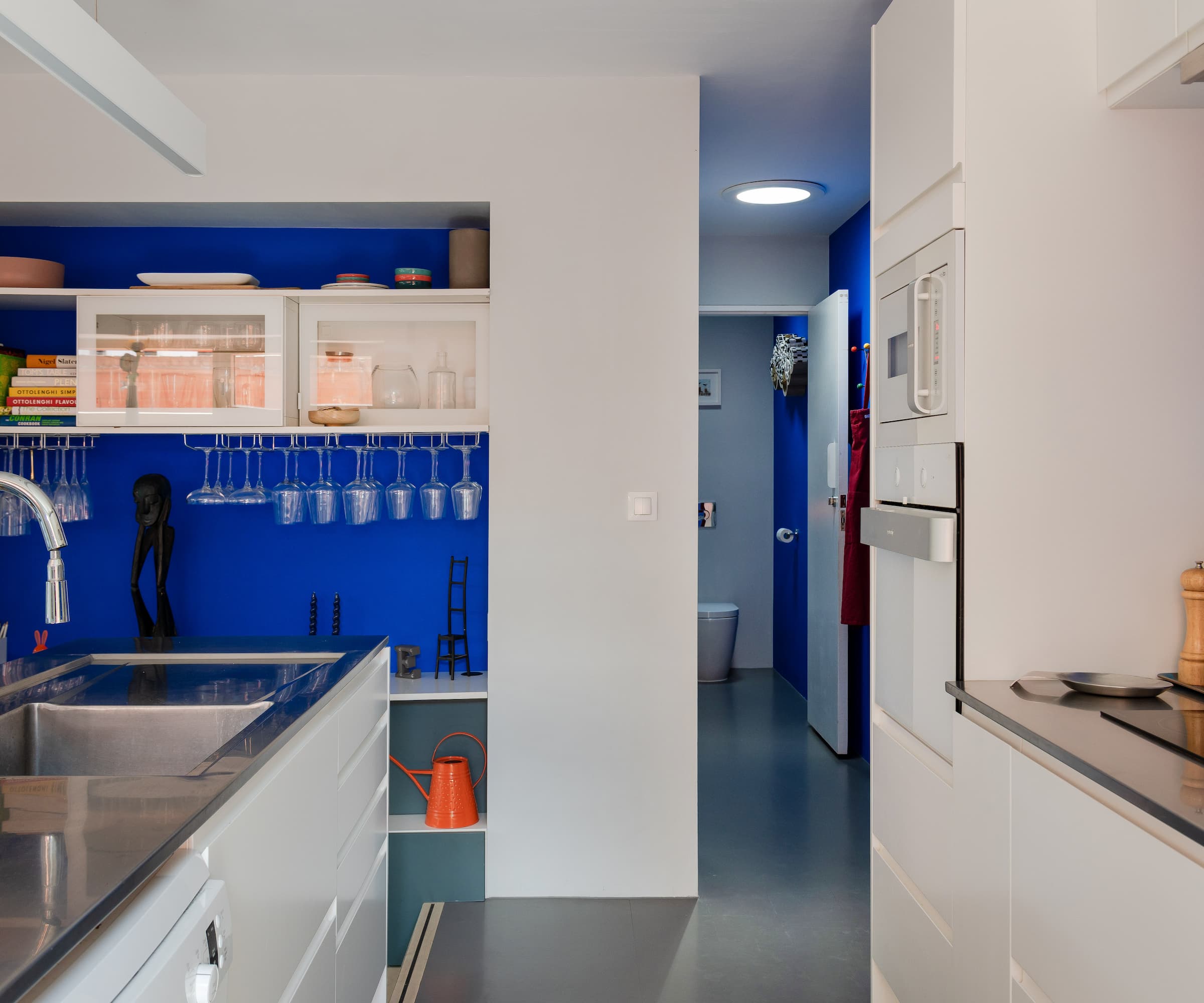 A kitchen with blue and white walls and a small hallway leading to a toilet room