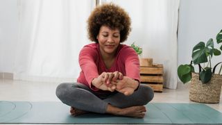 Woman sitting on yoga mat stretching with arms pushed forward