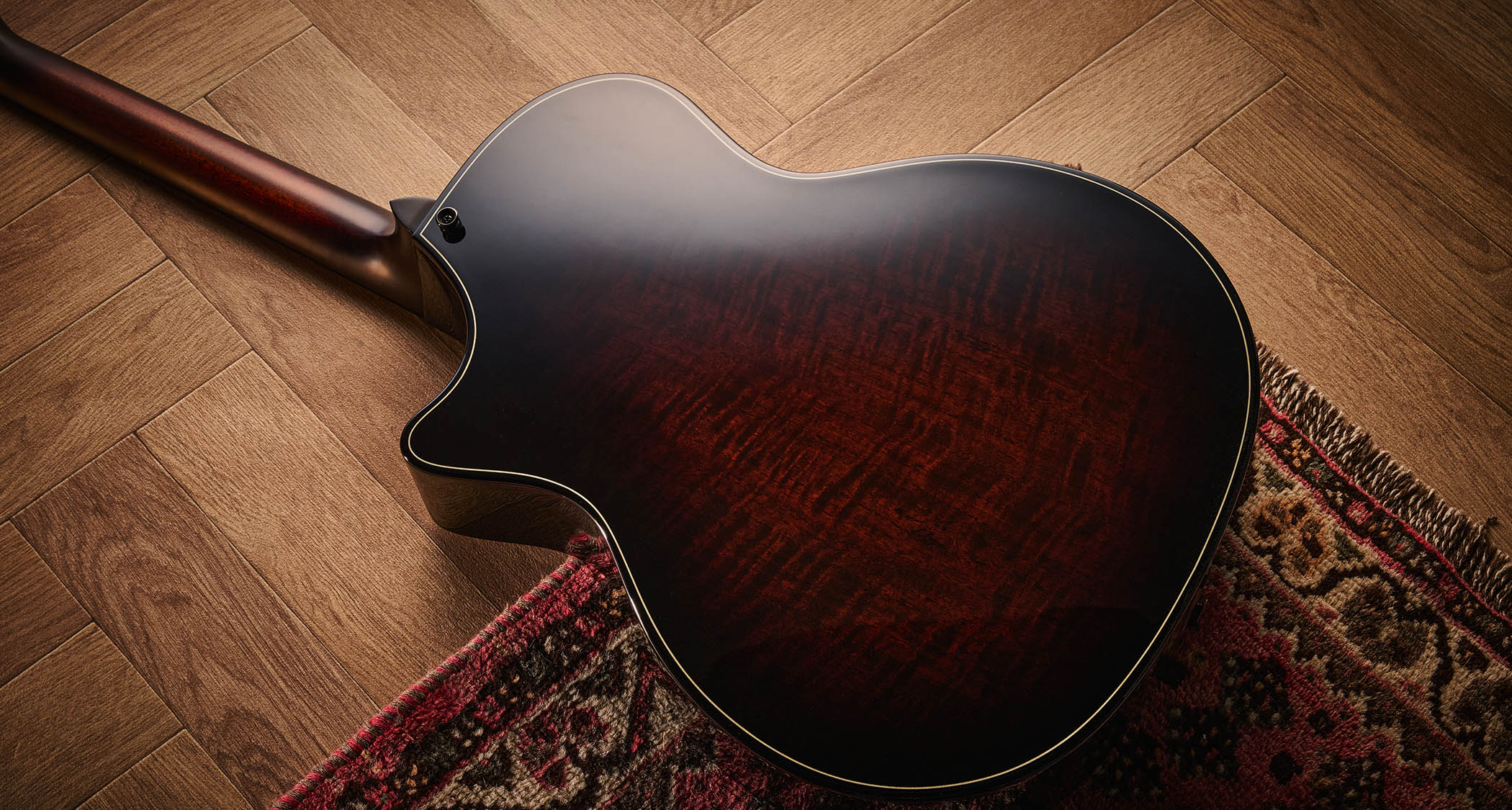 Taylor Builder’s Edition 514ce Kona Burst pictured against a wooden floor and patterned rug.