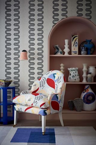 Textured monochrome patterned wallpaper in a snug with a colorful, abstract print armchair, blue and white rug and bookshelf.
