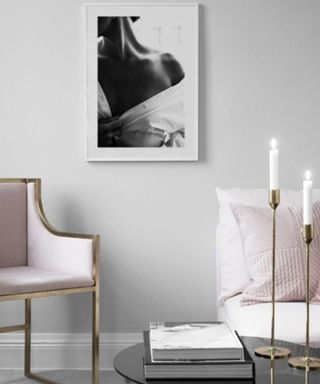 A black and white art print in a small living room with a chair and candles
