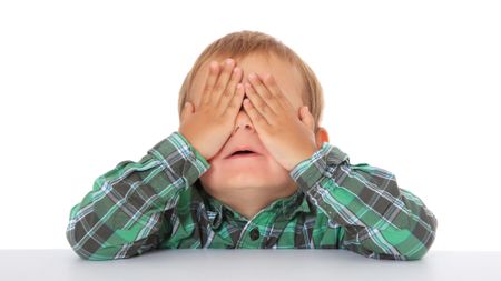 Studio portrait of a toddler in a plaid shirt covering his eyes with his hands