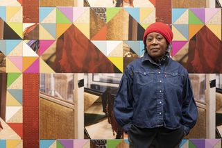 Sonia Boyce in front of colourful wallpaper, wearing blue hacket and red hat