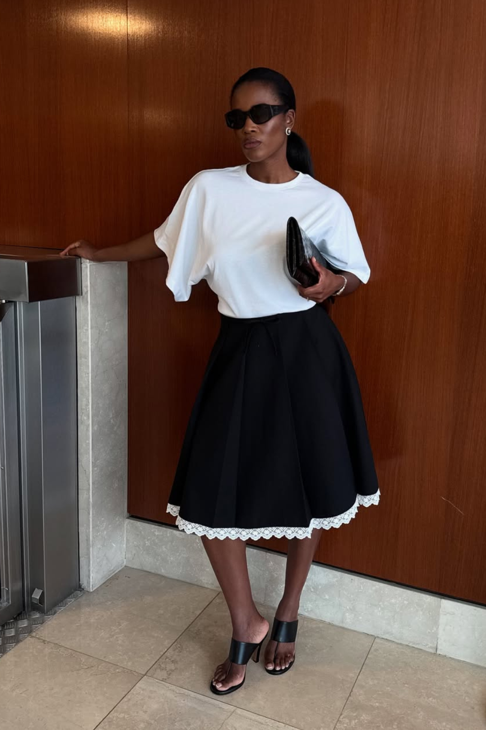 @nlmarilyn wears black skirt, white t-shirt, black sandals and sunglasses