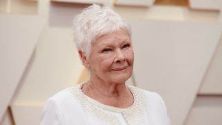 Image of Judi Dench smiling, with grey short hair in a pixie cut, and wearing a white pearl-embellished jacket