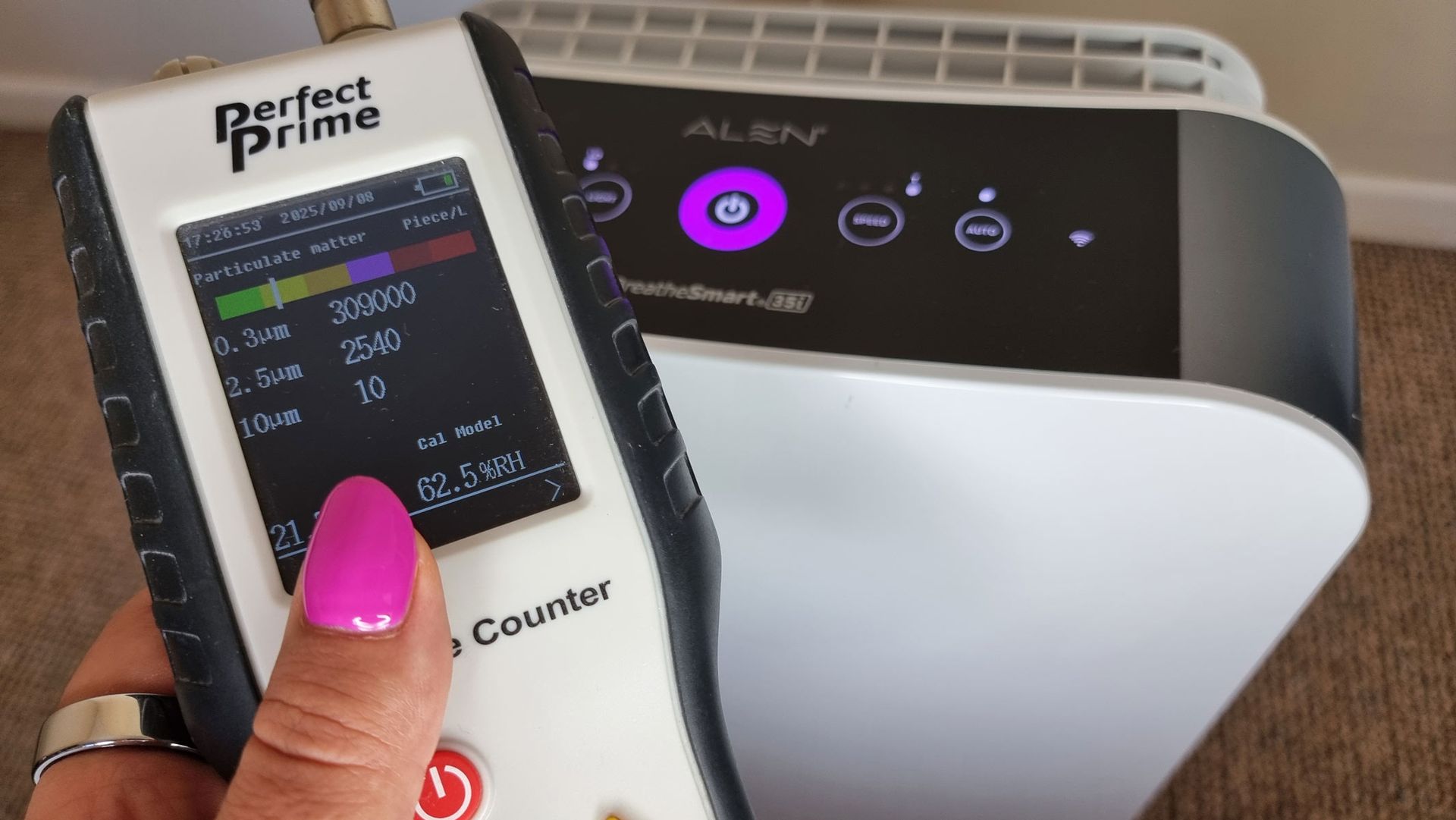 A picture of our reviewer holding the Perfect Prime air particle monitor in front of the Alen BreatheSmart 35i air purfier