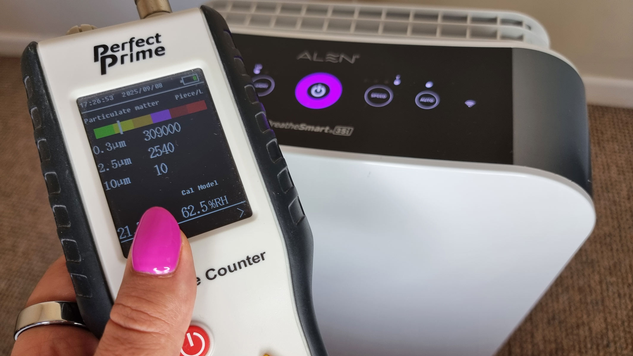 A picture of our reviewer holding the Perfect Prime air particle monitor in front of the Alen BreatheSmart 35i air purfier