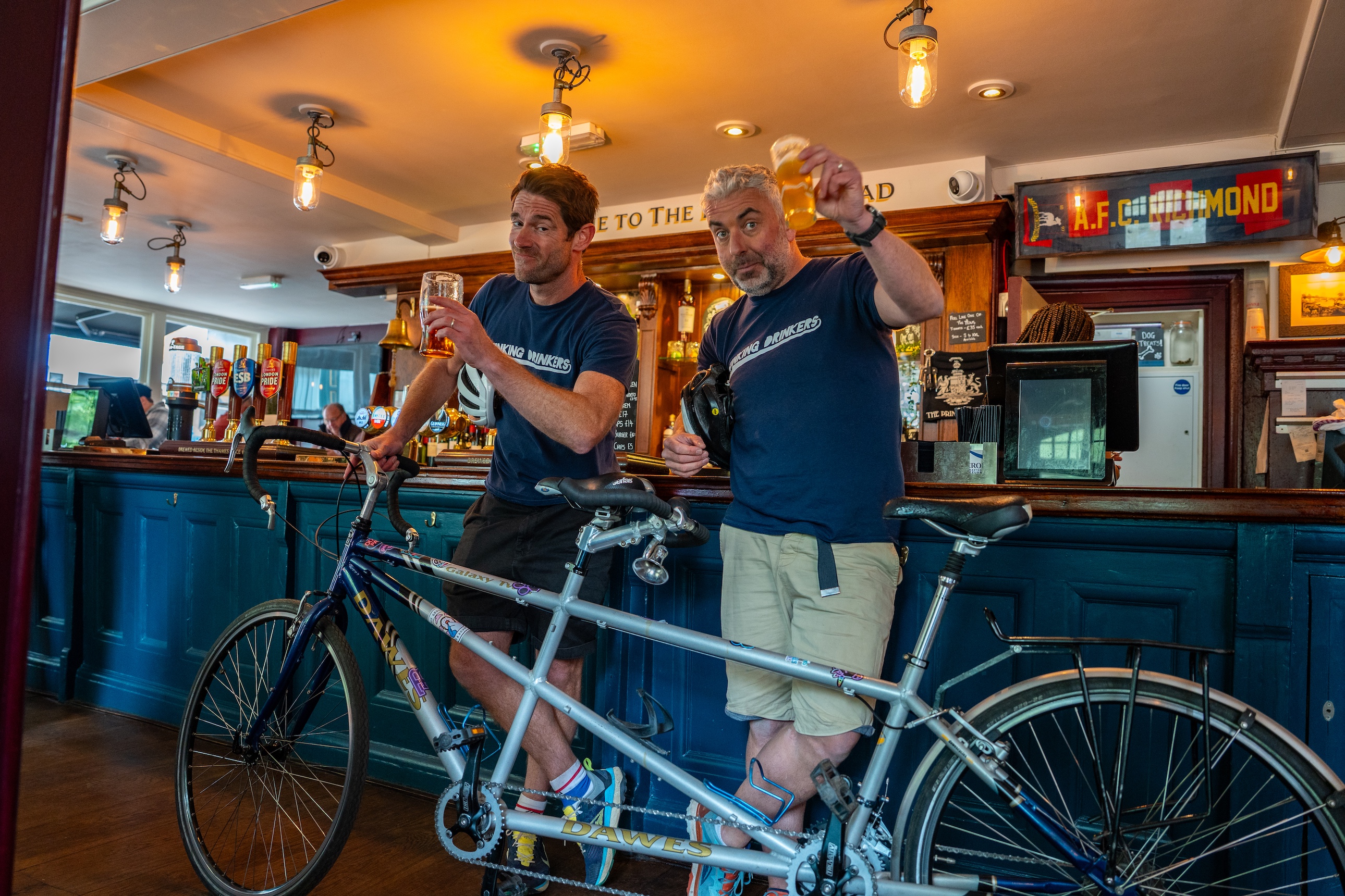 Ben and Tom in a bar with the tandem, raising a glass