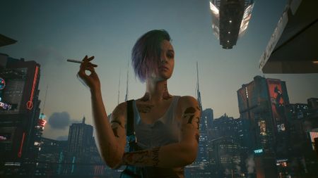 Cyberpunk 2077 screenshot showing Judy smoking a cigarette on the rooftop, with a vista of Night City illuminating the background behind her