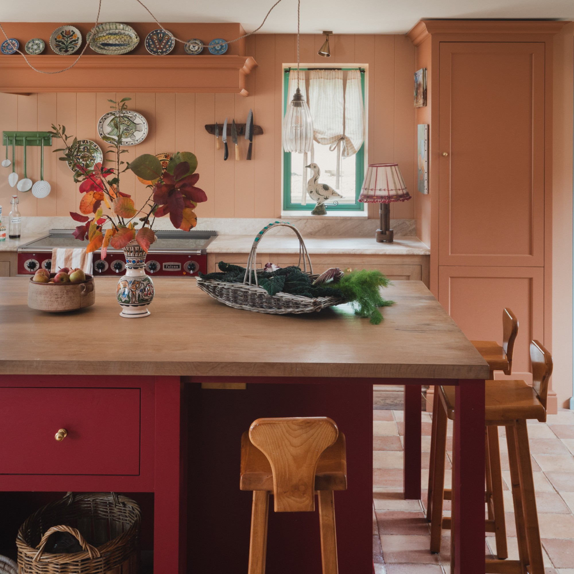 A kitchen painted in a terracotta shade with a red kitchen island and wooden stools