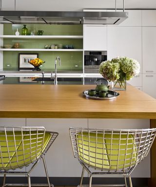 White kitchen with green backsplash and wood countertop island with barstools