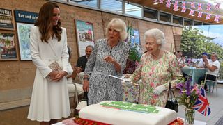 Queen Elizabeth prepares to cut a cake, watched by Queen Camilla and the Princess of Wales, to celebrate of The Big Lunch initiative at The Eden Project