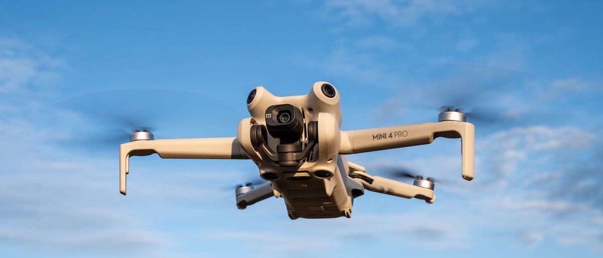 Yellow DJI Mini 4 Pro drone viewed from below flying across a blue sky.