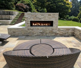 An outdoor fireplace built into a stone wall in a back garden with a day bed facing towards it