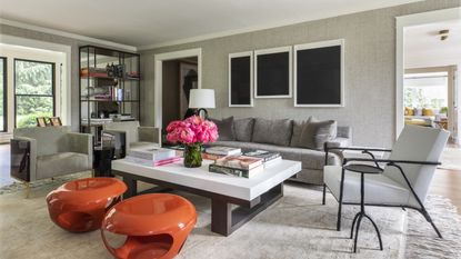 A grey living room with textured wallpaper, grey sofa and orange modern stools
