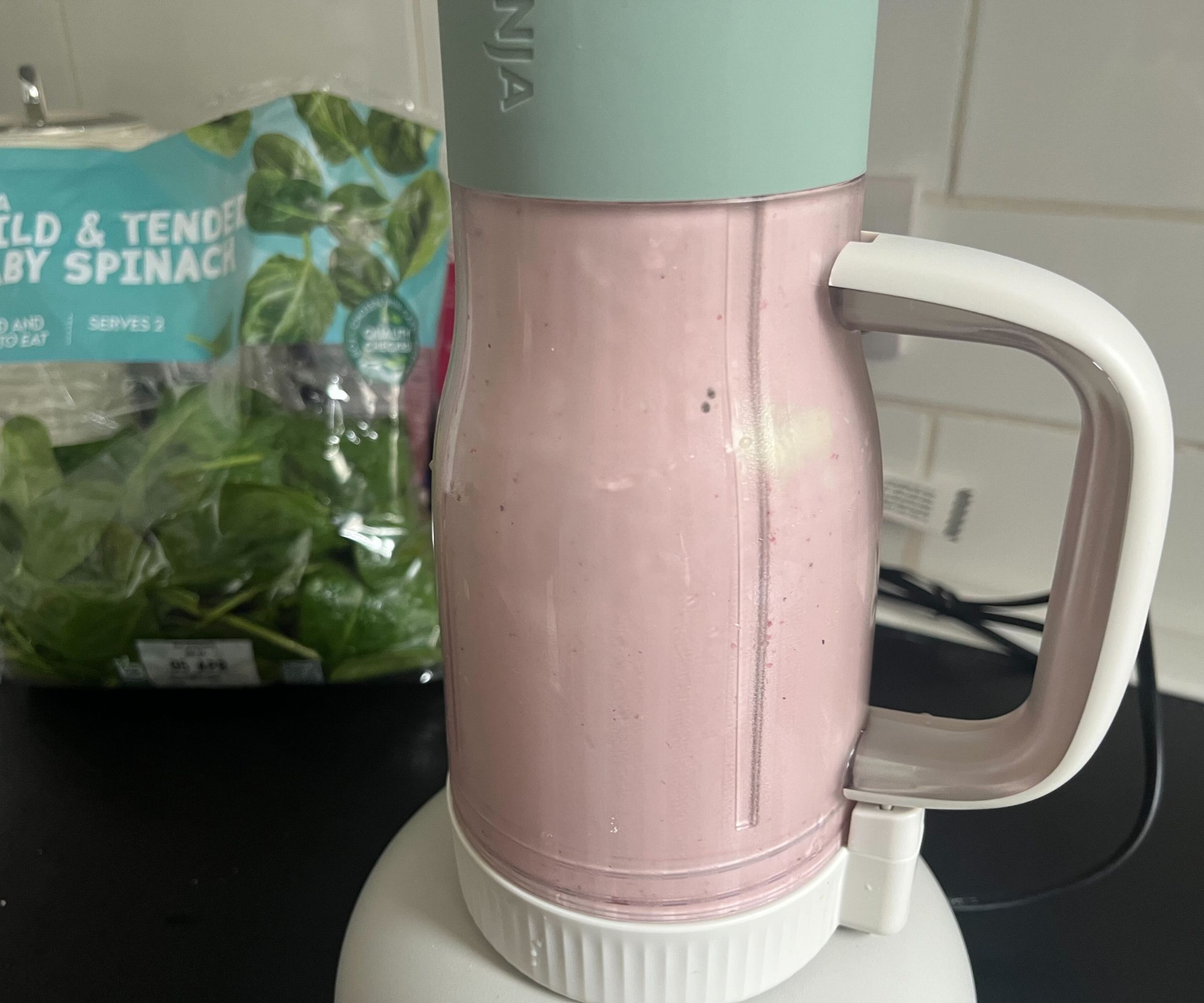 A blended pink smoothie in a Ninja Blendboss tumbler with a bag of spinach behind it. 