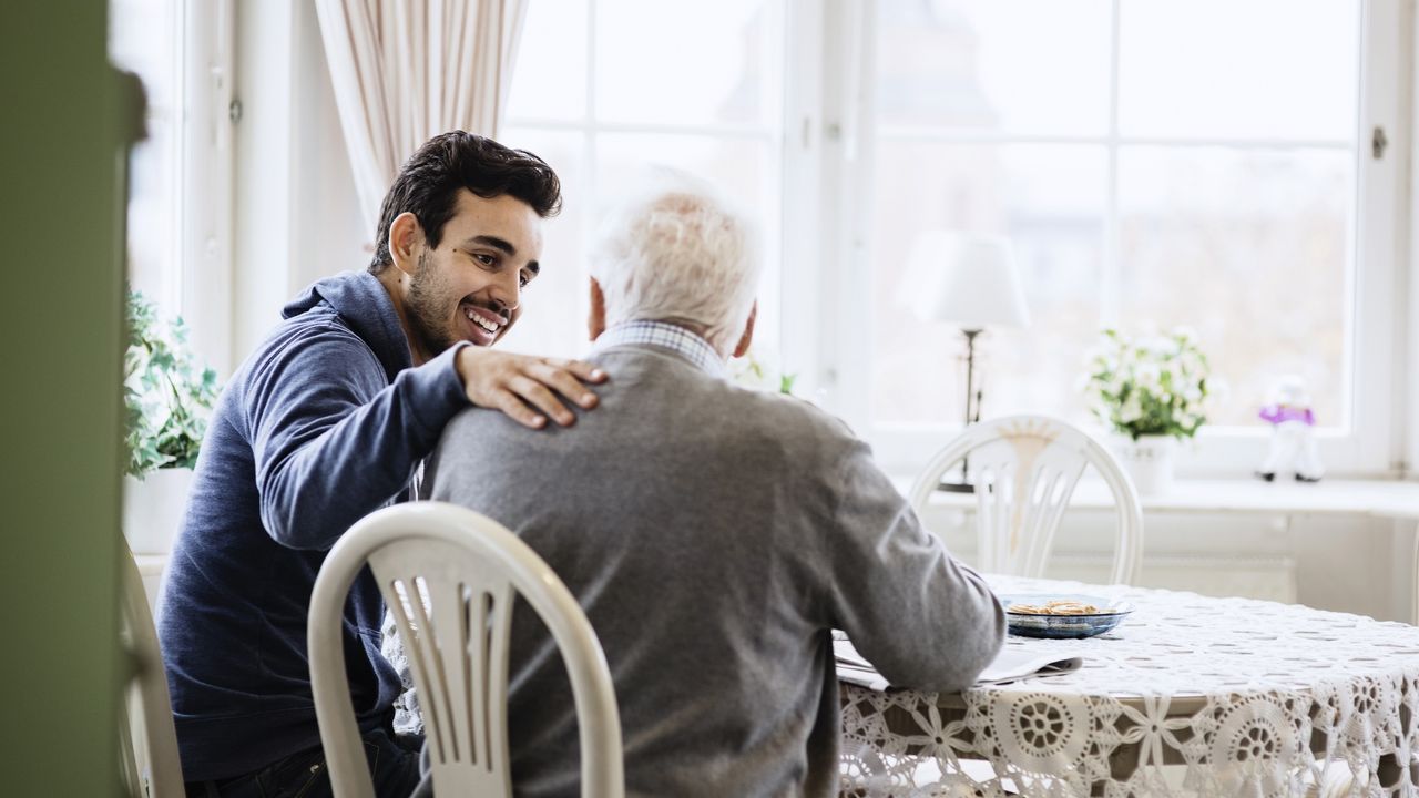 A son puts his hand on his father&#039;s shoulder as they have a discussion.