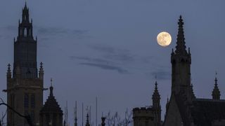 the full moon can be seen in the dusk sky above a city skyline