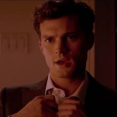 Jamie Dornan untying his shirt button in a scene from 'Fifty Shades of Grey'