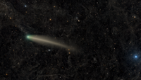 A comet is photographed glowing against a dusty deep-space starfield. 