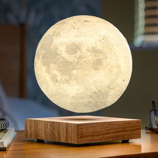 A levitating illuminated moon lamp above a wooden base