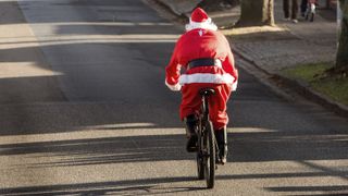 A cyclist dressed as Father Christmas rides a bike down an empty street