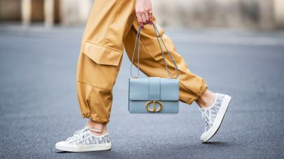 Closeup of the lower half of a woman wearing cargo pants walking while holding a purse.