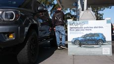 A vandalized sign about politicians, foreign oil, and gasoline taxes shows "Sacramento" crossed out and replaced with "Trump" reading, "Trump Policies Did This. Now You Pay More" is seen as a driver fuels a pickup truck at a Chevron gas station in El Segundo, California, on April 27, 2026. The US Treasury Department said on April 14 that it does not plan to renew a temporary easing of sanctions on Iranian oil that aimed to ease war-related supply shocks. (Photo by Patrick T. Fallon / AFP via Getty Images)