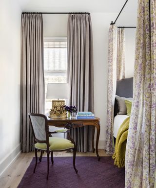 Bedroom window with drapes and grass shade, desk and chair in front and bed to one side