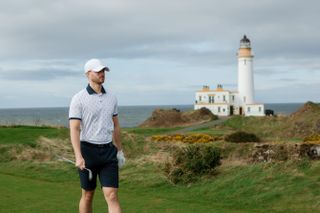 A golfer on a course with a lighthouse in the background