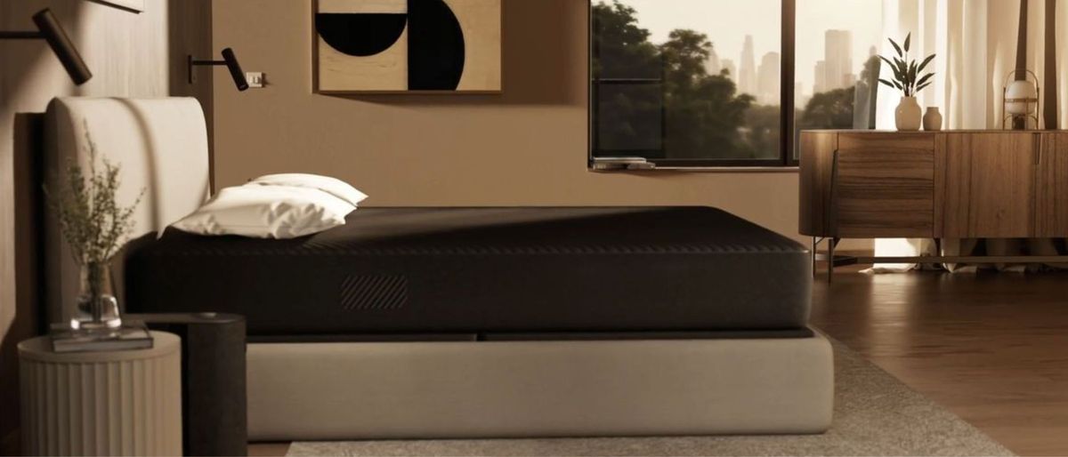 The image shows the Eight Sleep pod on a beige bed foundation, placed in a neutrally decorated bedroom