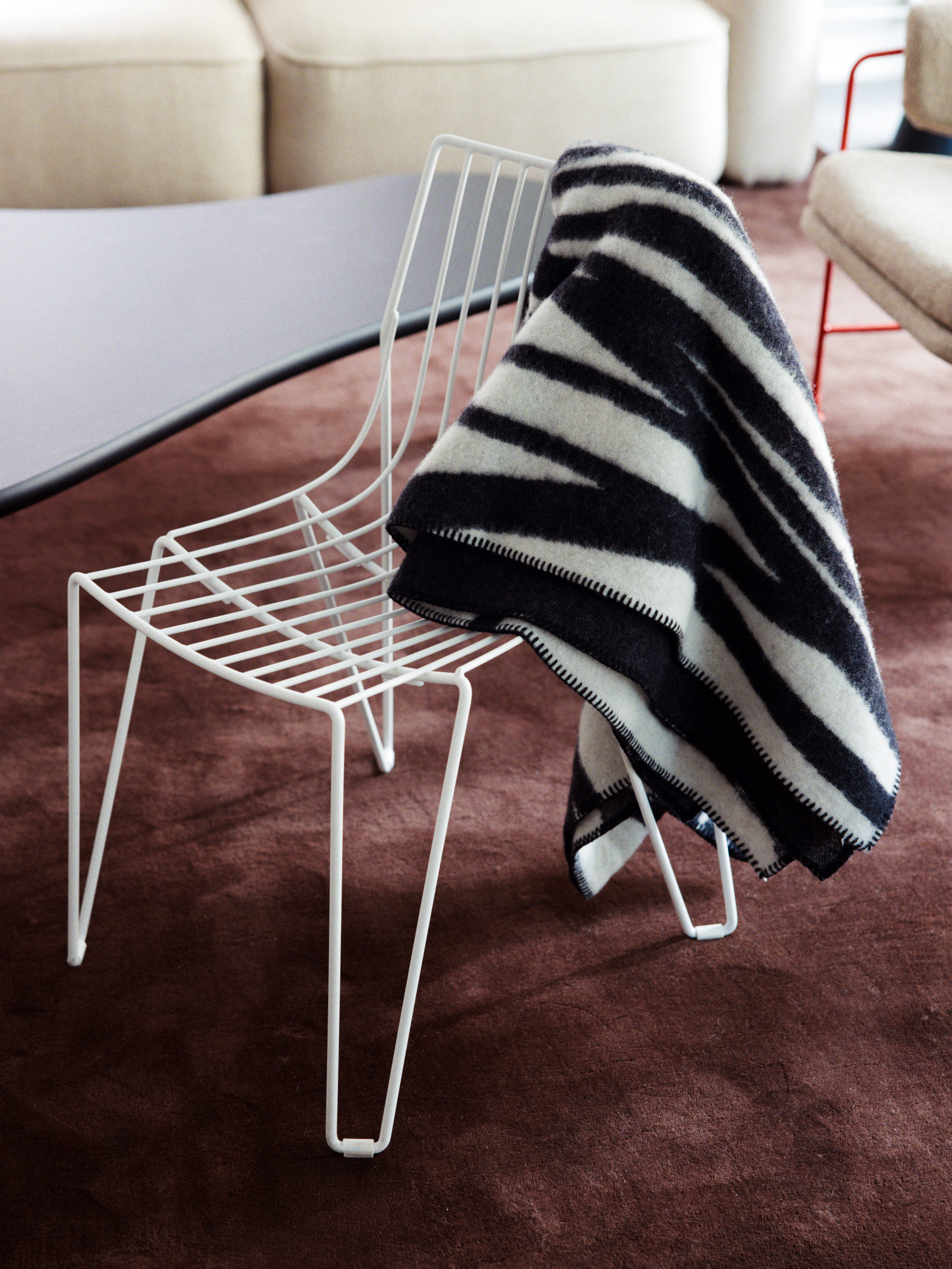Image of a white wire chair with a black and white throw blanket on it on a dark brown rug.