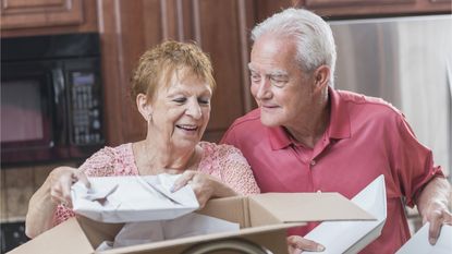 An older couple unpack dishes in a kitchen.