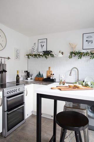 A white kitchen with monochrome kitchen island with round bar stool and Christmas foliage on shelves