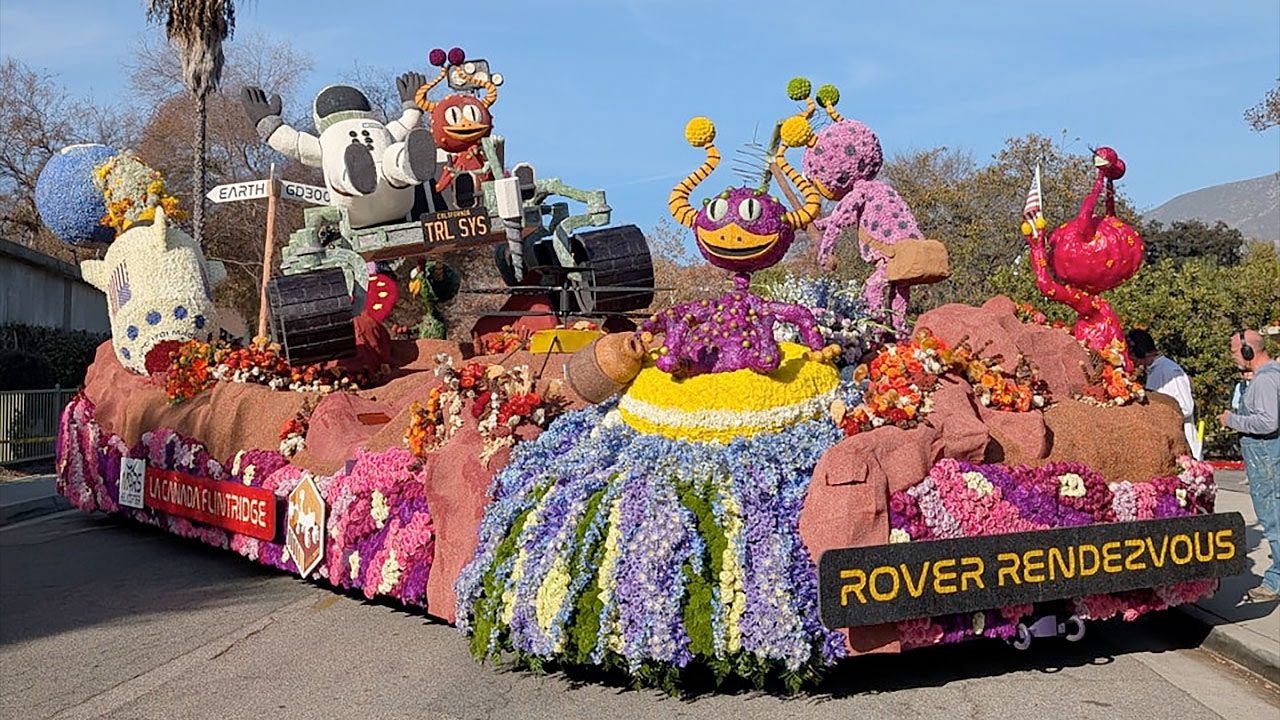 flower-covered parade float depicting an astronaut and a family of aliens on mars