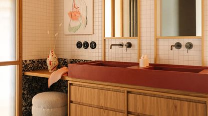 mid century modern inspired bathroom with terrazzo floors, red sink, timber vanity with storage, two wall mirrors with built-in light, chrome taps, an artwork, white square tile walls, and an ottoman vanity station