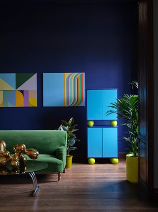 Rainbow paintings and green velvet sofa against a dark blue wall