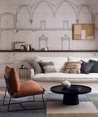 A neutral living room picture with architectural mural walls, cream sofa and orange armchair.