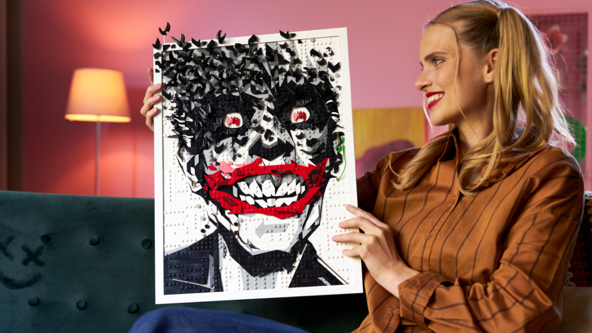 A woman smiles while holding up and looking at a Lego Joker set in a frame
